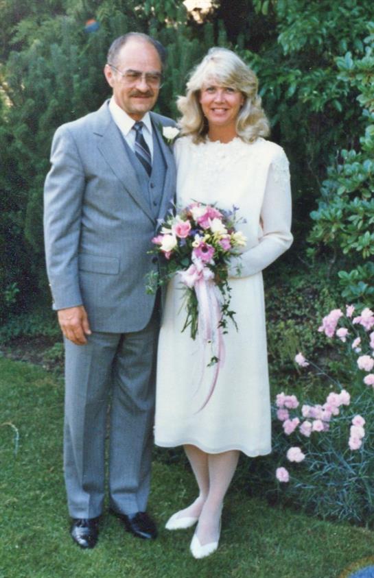 A smiling couple in formal attire stands together, ready to celebrate their garden wedding.