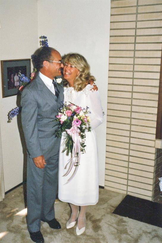 Happy couple in wedding attire hugs amidst floral decor and warm ambiance.