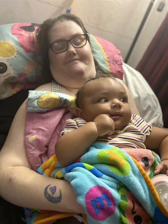 A mother holds her baby in a warm and comfortable bedroom, both relaxed and happy together.