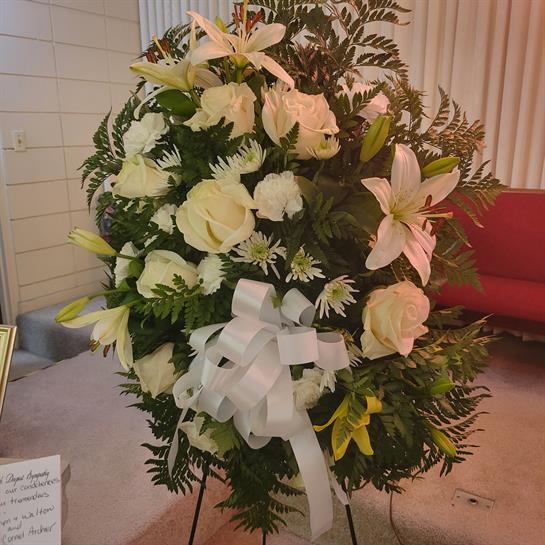 A lovely floral tribute of white roses and lilies with green ferns in a solemn setting.