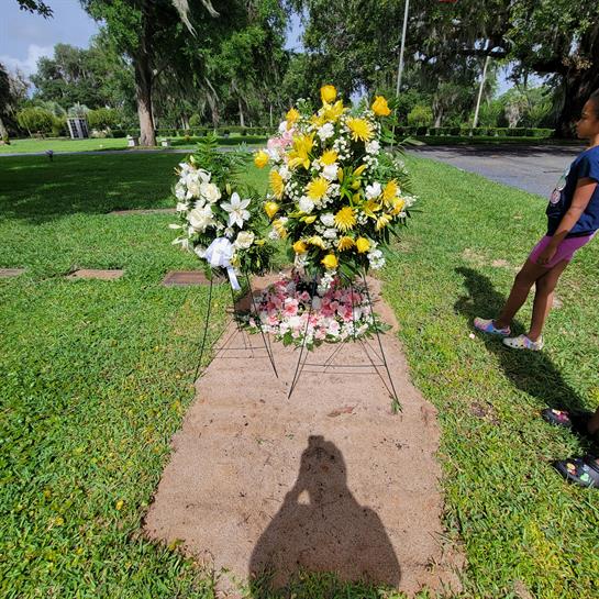 Family member places flowers at a gravesite in a serene cemetery during a sunny day.