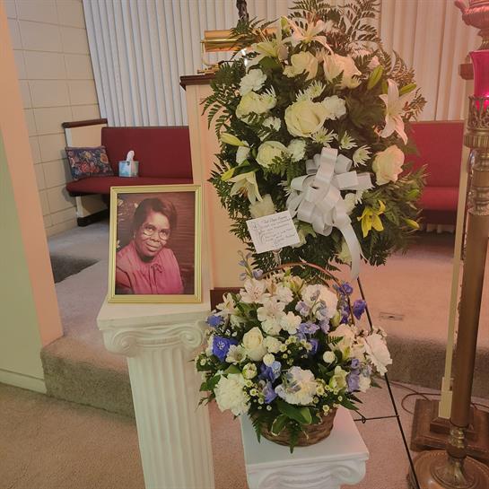 Floral arrangements surround a framed picture in a church, honoring a recently passed loved one.