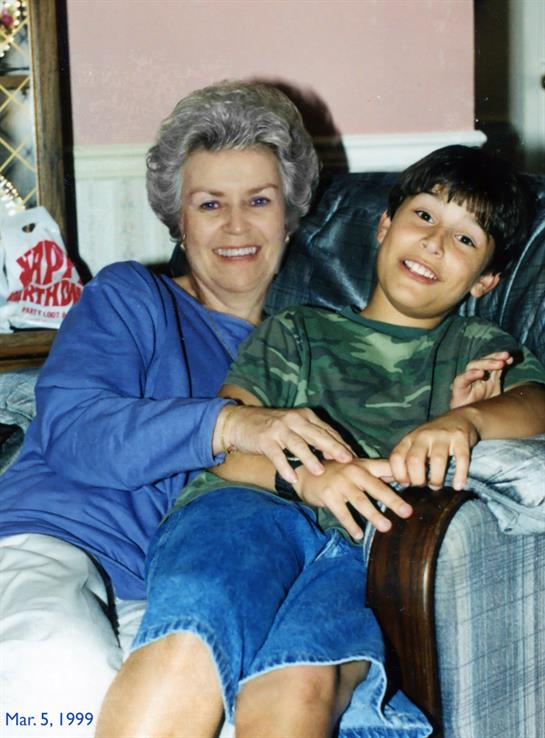 An elderly woman and her grandson enjoy their time together, smiling on the sofa at home.