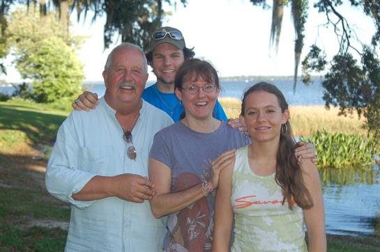Four family members share laughter and smiles while enjoying a sunny day near the water.