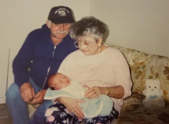 Grandparents are lovingly cradling their newborn grandchild while sitting on a couch.