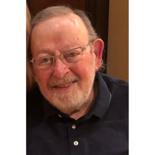 Elderly man with glasses and a beard smiles warmly while seated in a relaxed atmosphere.