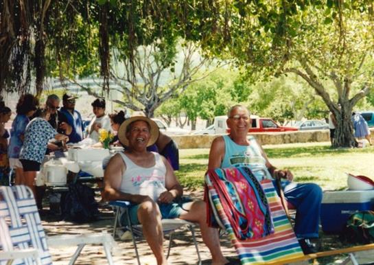 Friends relax together in a park, sitting on chairs and sharing laughter under the shade of trees.