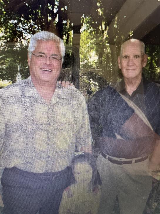 Two men enjoy their time together outdoors, smiling and standing close in a vibrant garden.