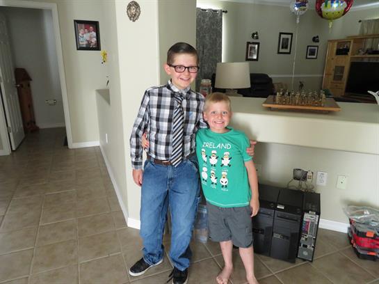 Two boys smile in a cozy living room, flaunting their contrasting outfits.