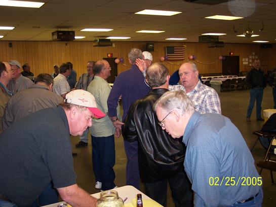 Group of older men interact and socialize at a community event in a spacious hall.