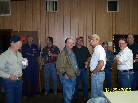 A group of men stands in a cozy room, chatting with drinks in hand, enjoying a casual gathering.