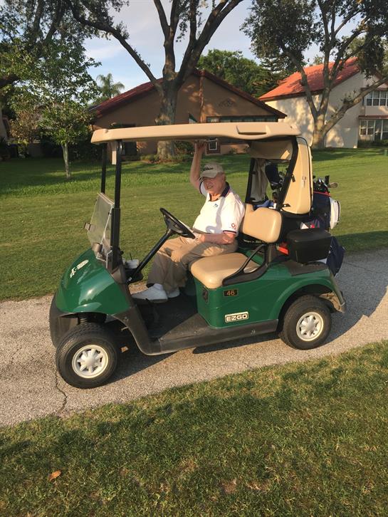 A cheerful driver waves while enjoying a sunny ride on a golf cart.