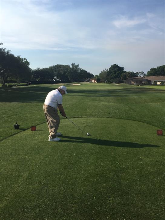 A golfer prepares to hit the ball from the tee area at a driving range under clear skies.