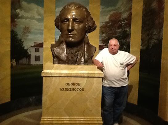 A visitor stands beside a large bronze bust of George Washington in a museum.