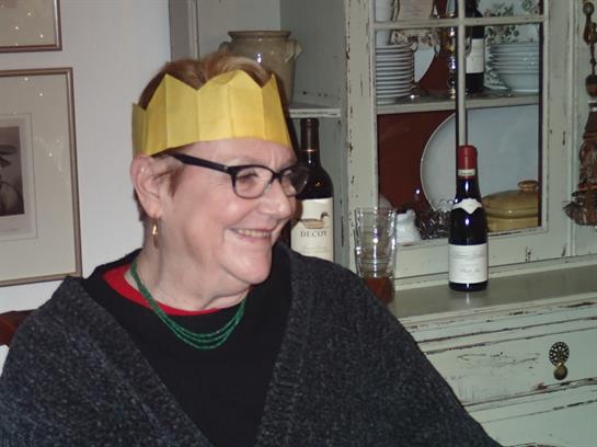 The woman enjoys a joyful moment at a holiday gathering, dressed warmly with a festive crown.