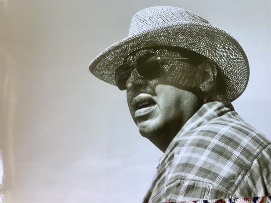 An actor with sunglasses and a straw hat enjoys a bright day outdoors, exuding charisma.
