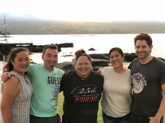 Group of friends smiling and posing for a picture by the beach during sunset, enjoying their time.