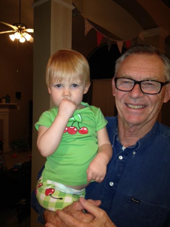 A smiling grandfather holds his thumb-sucking granddaughter in a cozy family setting.