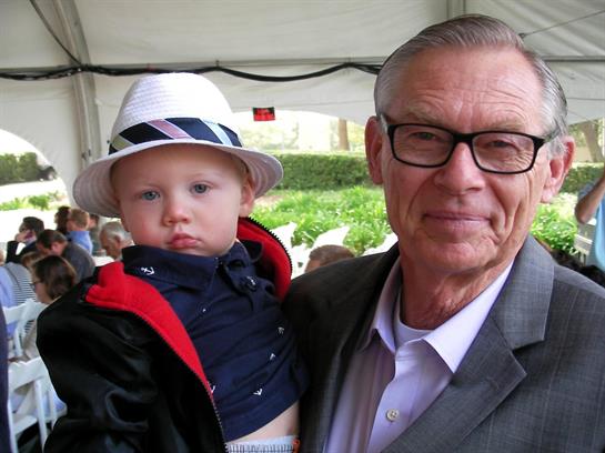 A man proudly holds a young child in a festive outdoor setting during a family event.