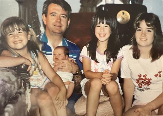 A family enjoys a warm gathering, featuring children smiling alongside adults in a living space.