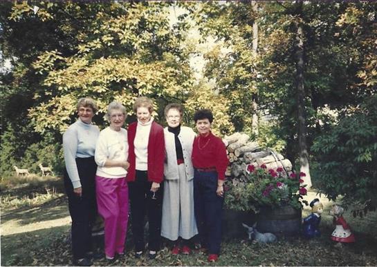 Five women gather in a vibrant garden, sharing laughter and joy on a sunny day.