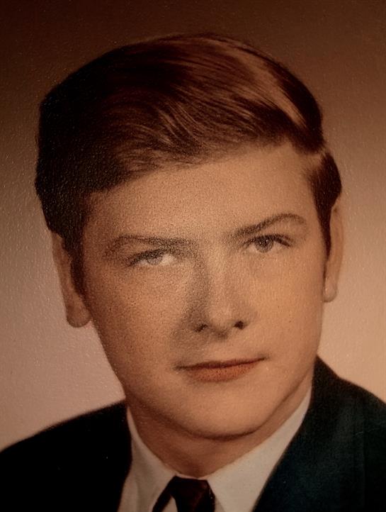 A young man in a suit displays his hairstyle and serious expression from the 1960s.