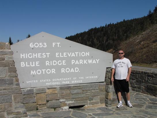 A person poses next to a stone sign indicating the highest elevation on Blue Ridge Parkway.