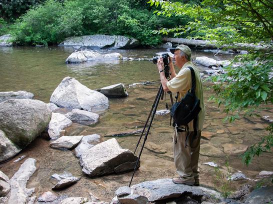A photographer adjusts gear by the riverbank to capture the serene waters and nature.