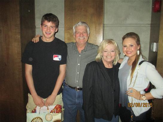 Four family members stand together, smiling, enjoying their time in a warm indoor environment.