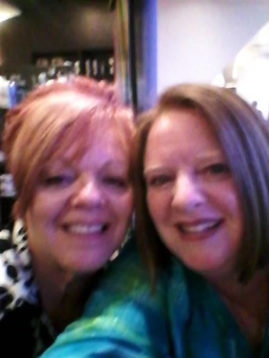 Two women smile brightly while enjoying each other's company in a warm setting.