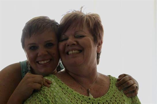 Two happy women embrace each other, showcasing their joyful expressions in a well-lit setting.