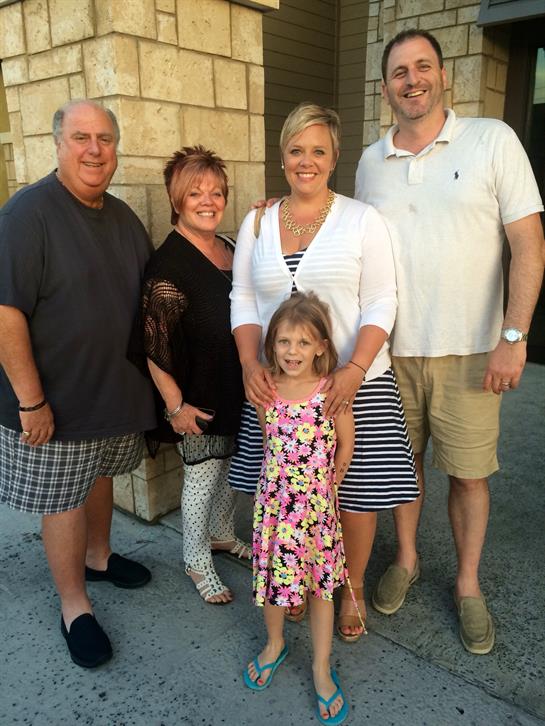 Group of five people enjoying a summer evening, posing warmly together outside a building.