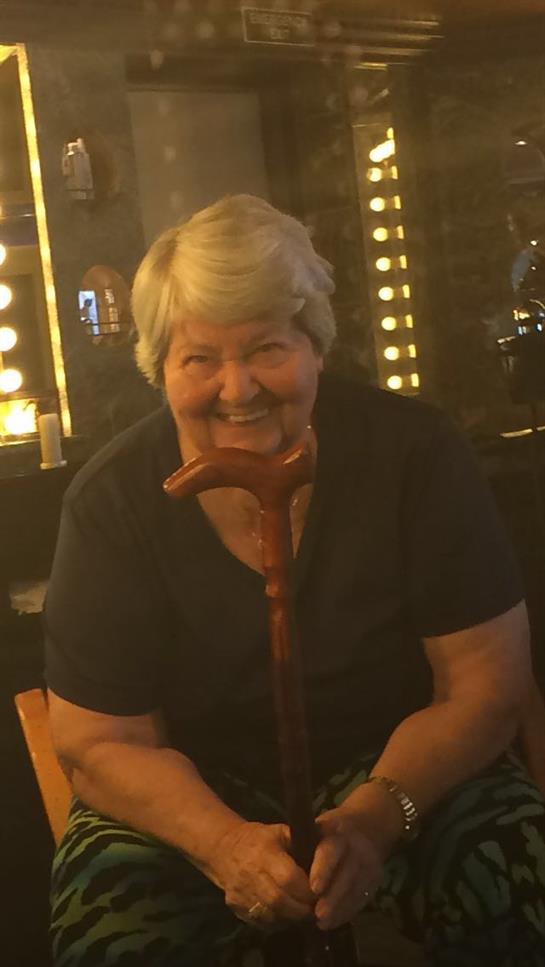 An elderly woman with a warm smile is seated, holding her cane in a welcoming atmosphere.