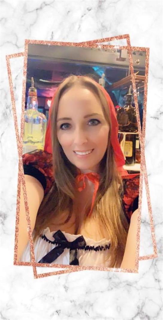 A woman smiles while dressed in a red hooded costume, enjoying a festive atmosphere.