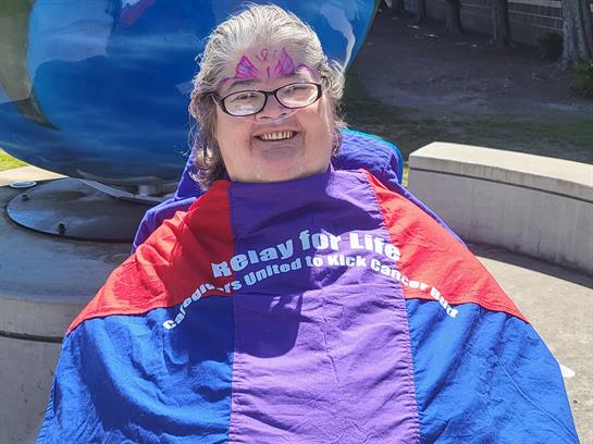 Woman in colorful blanket spreads joy at local event supporting cancer research.
