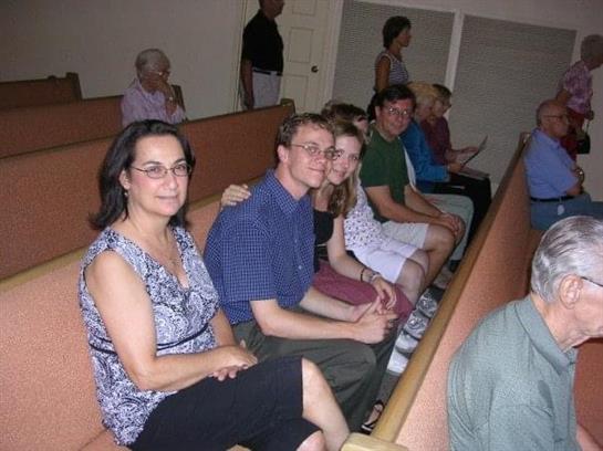 Friends smile and chat while seated in a community hall, enjoying an event or gathering.