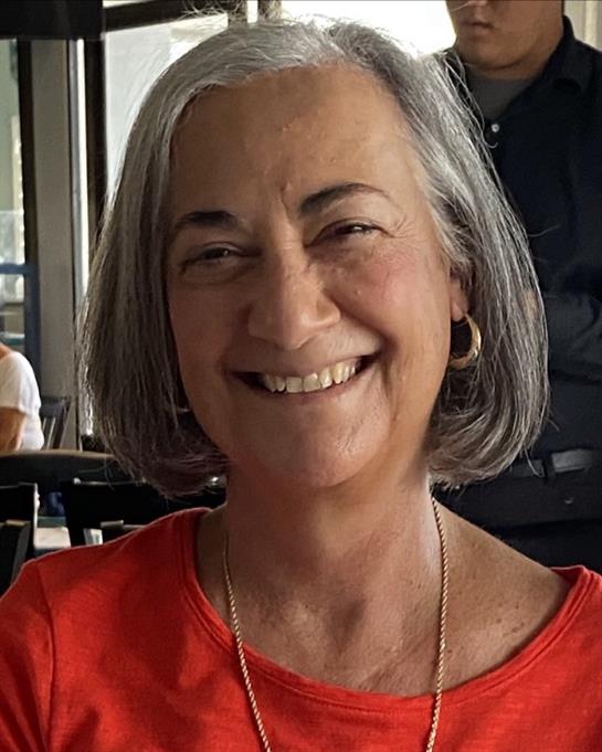 A joyful woman with gray hair is smiling warmly, sitting in a casual cafe setting.