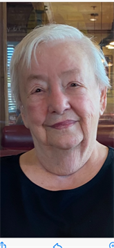 An elderly woman sits happily in a casual restaurant, enjoying her time with a warm smile.