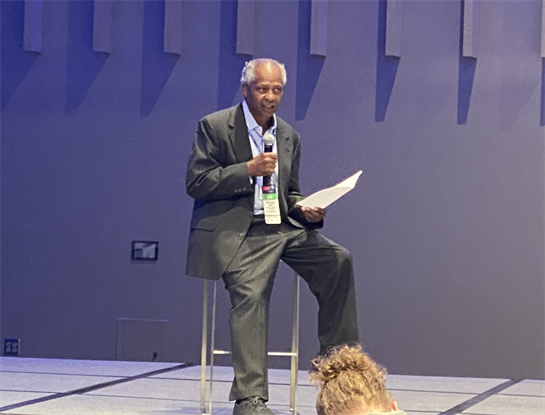 A speaker shares valuable insights while seated on a stool in a contemporary conference setting.
