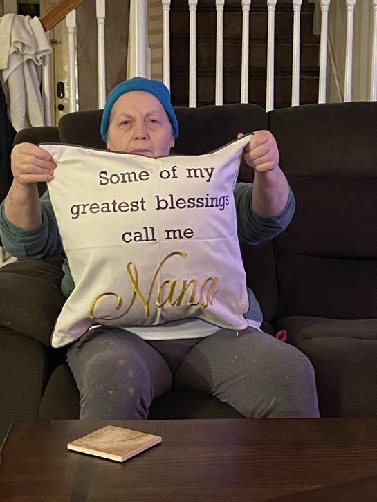 A person sits on a couch proudly displaying a pillow that celebrates family ties.