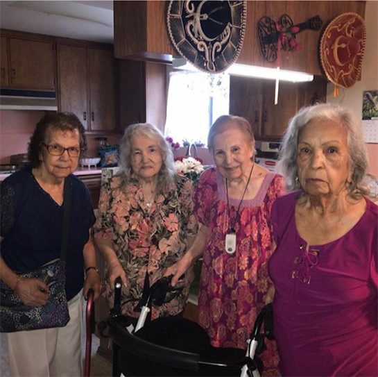Four elderly women share joy in a warm kitchen adorned with colorful decorations.
