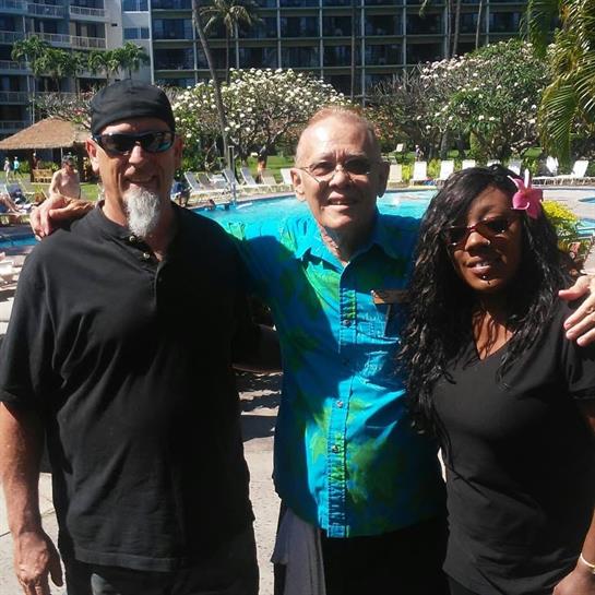 Three friends pose happily together by the pool at a tropical resort under blue skies.