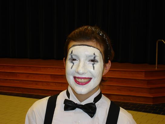 A young performer with white face paint and a bow tie expresses joy while on stage.