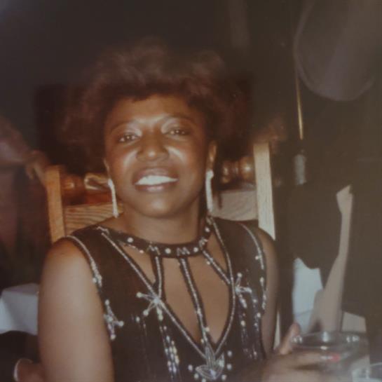 A woman smiles brightly while holding a drink at a lively celebration.