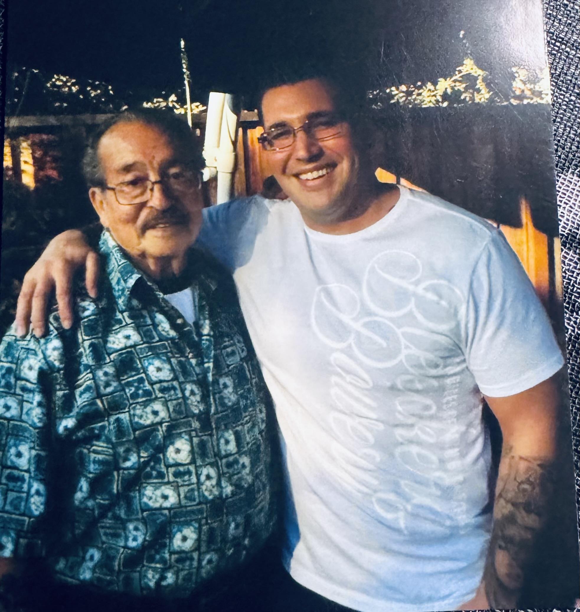 Two men stand close, smiling warmly with family ties evident in their expressions.