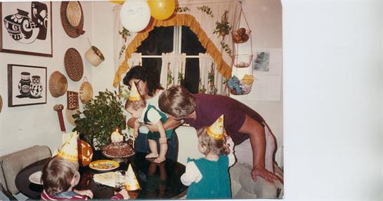 Family members enjoy a festive birthday gathering with children wearing party hats and decorations.