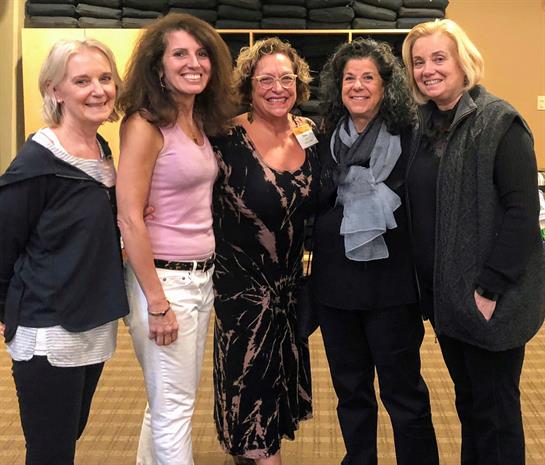 Five women pose together, showcasing joy and friendship at a community event in the evening.