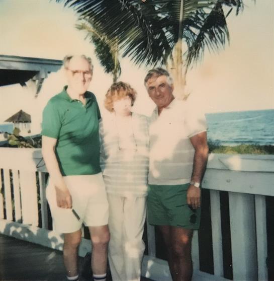 Three friends pose on a deck by the ocean, enjoying great company and warm weather.