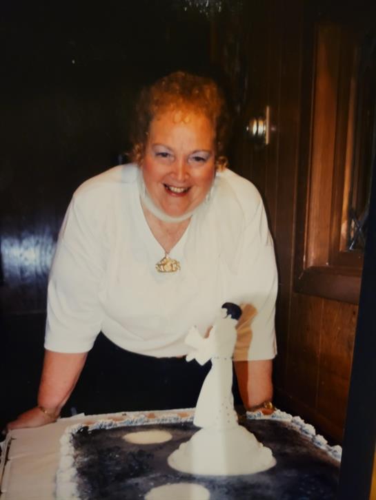 A joyful woman leans over a beautifully decorated cake, smiling widely in celebration with guests.