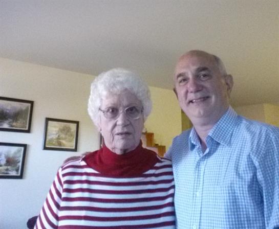 A young man poses beside his grandmother in a cheerful living room filled with family memories.